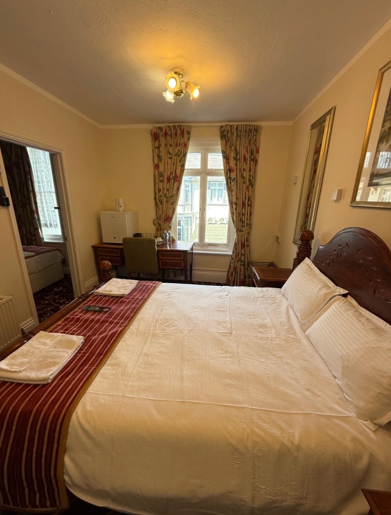 Family room with large bed, maroon runner, dark wood furniture, and adjoining room at The Queens Road Hotel