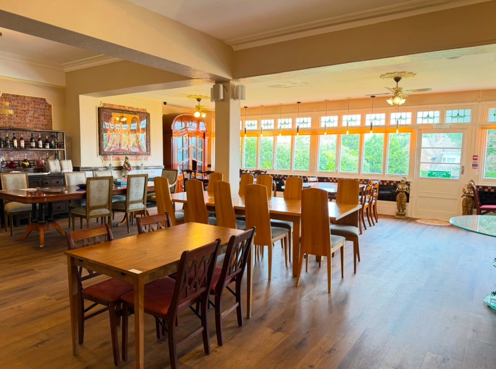 Bright restaurant interior with wooden flooring, varied seating, and natural light from garden-facing windows