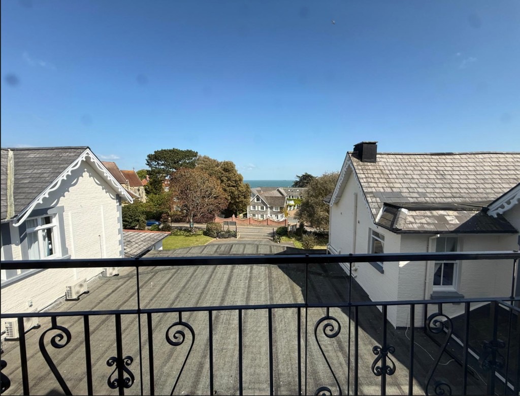 Sea and neighbourhood view from a balcony at The Queens Road Hotel, with white buildings and greenery under a clear blue sky