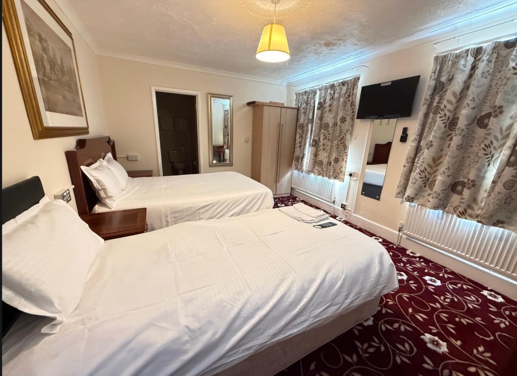 Triple room with double and single beds, ensuite bathroom, and wooden furniture at The Queens Road Hotel